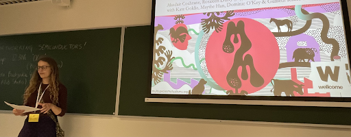 A speaker standing in front of a presentation that features the Multispecies Mutualisms logo.